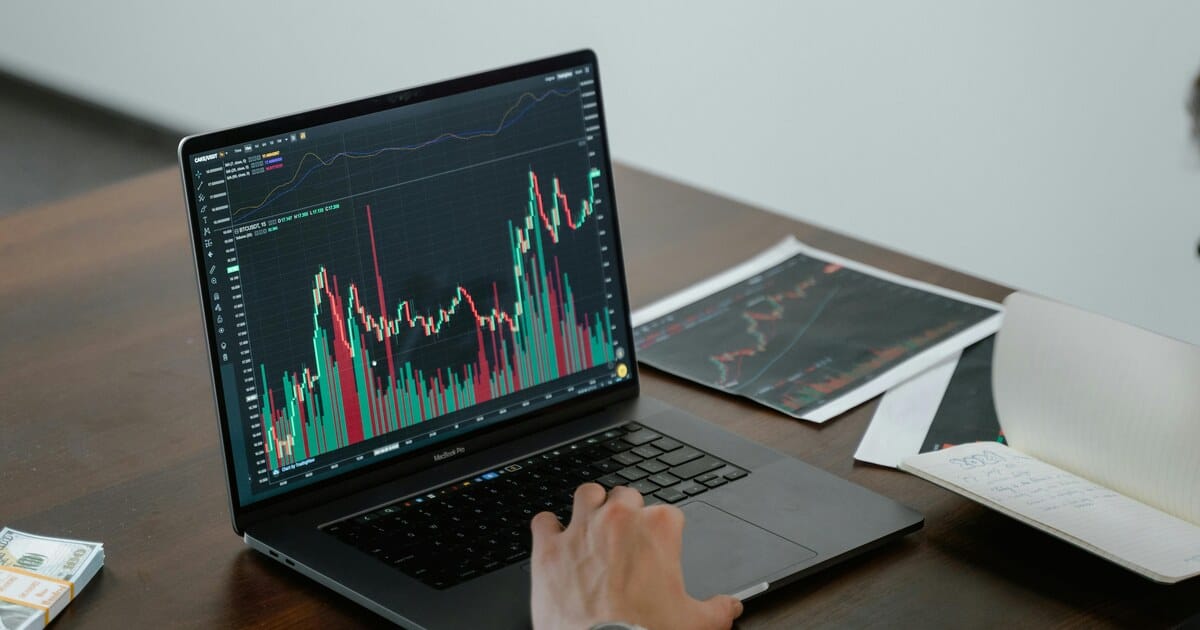 Analyst reviewing market charts on laptop in a trading setup.